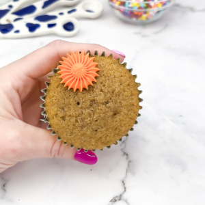 Piping orange buttercream dot onto the edge of a chocolate cupcake with a star tip.
