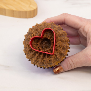 A heart shaped cookie cutter being used to make a shape in the chocolate buttercream mane. Step 4.