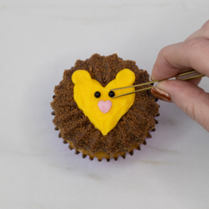 Using tweezers to add a face on the lion cupcake. Step 8.