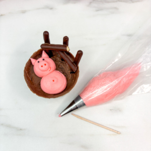 Adding snout, ears, and details to pig faces with smaller piping tip and sprinkles
