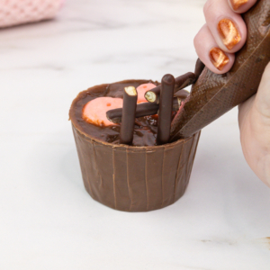 Pouring chocolate ganache into cupcake pots to create mud effect