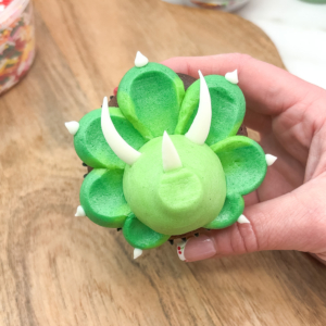 Adding candy melt horns to the face on a dinosaur cupcake. Step 8.