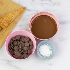 Bowls of melted chocolate, chocolate melts, and vegetable shortening on a marble surface, showing how to thin chocolate for dipping sugar cones