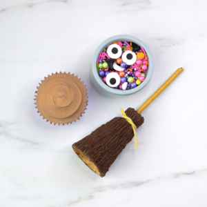 Flat lay of broomstick, sprinkles and chocolate cupcake