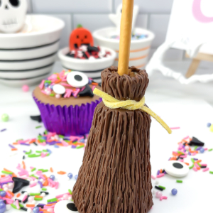 Finished chocolate broomstick cupcake with a yellow sour strap tie and colourful Halloween sprinkles in the background.