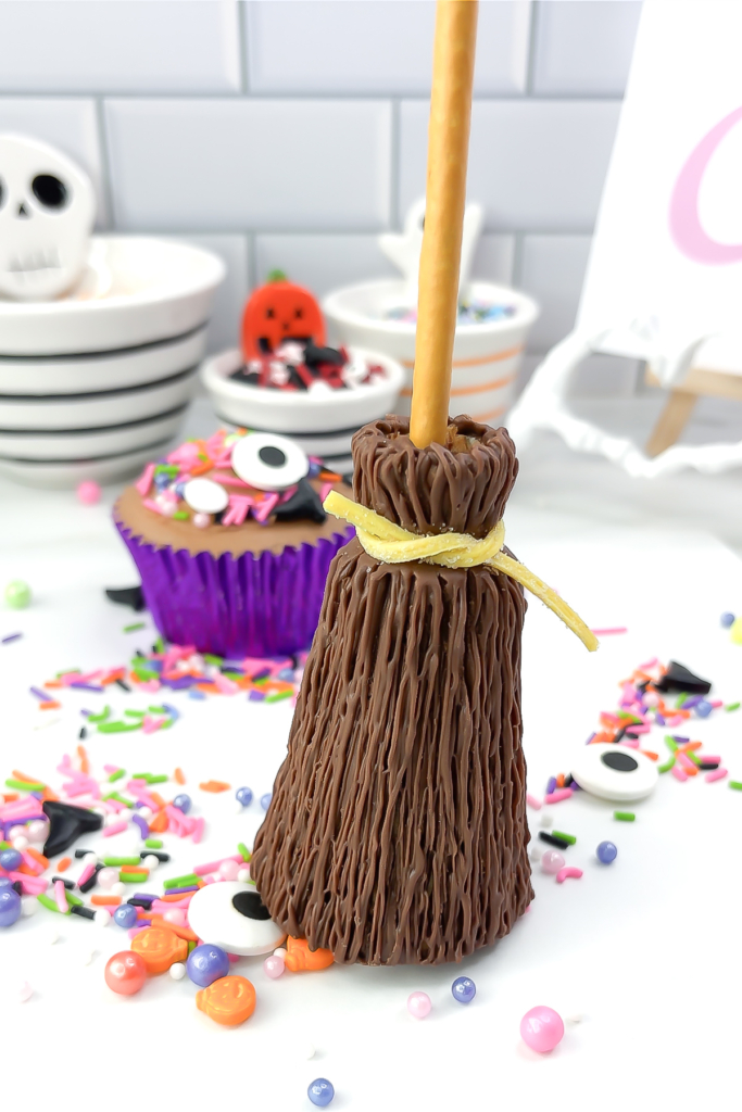 Finished chocolate broomstick cupcake with a yellow sour strap tie and colourful Halloween sprinkles in the background.