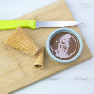 Cutting the pointed tip off a sugar cone with a serrated knife, bowl of chocolate.