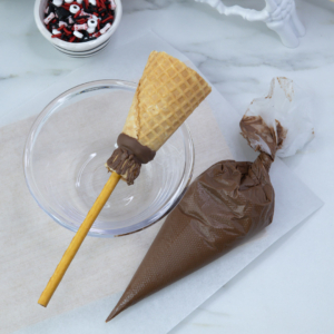 Piping chocolate drizzle on the narrow end of the cone to create broom bristles.