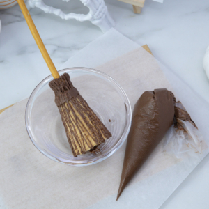 Piping chocolate drizzle on the large end of the cone to create broom bristles.