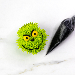 Green fur cupcake beside a piping bag filled with black buttercream for facial features.