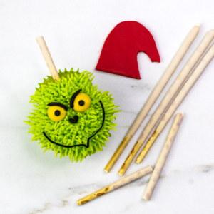 Grinch cupcake with pocky stick support and red fondant hat piece beside it.