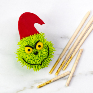 Grinch cupcake with the red fondant Santa hat attached, shown with pocky sticks on the side
