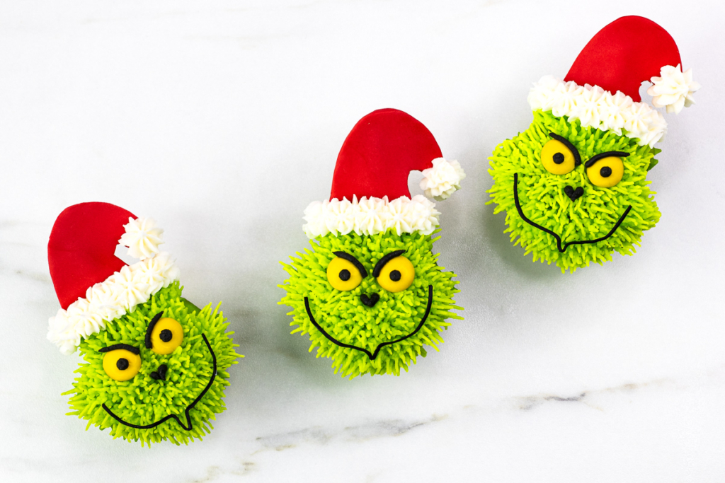 Three completed Grinch cupcakes arranged diagonally with Santa hats and bright green buttercream fur.
