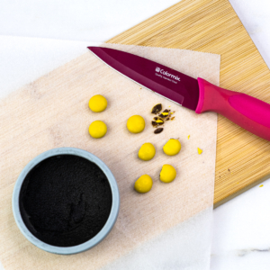 Yellow chocolate balls cut in half beside a bowl of black buttercream and a knife