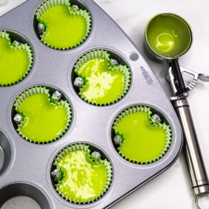 Green cupcake batter in liners shaped with two foil balls to form the Grinch head silhouette.