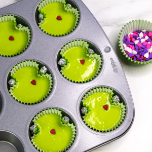 Green cupcake batter shaped with foil balls and topped with a single red heart sprinkle