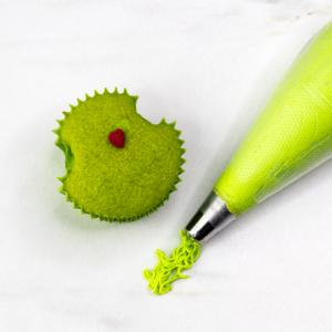 Grinch cupcake with the buttercream and piping bag next to it.