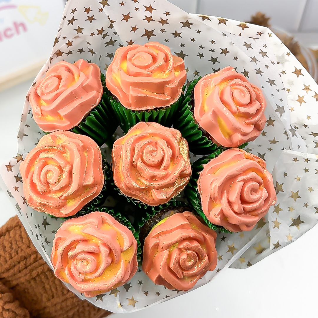 Overhead view of a rose cupcake bouquet wrapped in star-patterned tissue paper, showing the peach and yellow two-tone roses.”