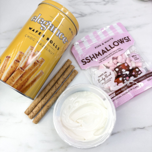 Flat lay of wafer sticks, mini marshmallows, and a bowl of melted white candy melts on a marble background — ingredients for the turkey leg cupcake bones.