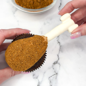 Inserting the candy melt bone into the end of the cupcake to finish the turkey leg design