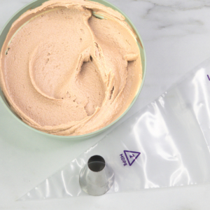 Bowl of light brown buttercream beside a piping bag fitted with a large round piping tip, ready to pipe the turkey leg cupcakes