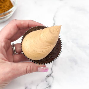 Piping brown buttercream onto a chocolate cupcake in the shape of a drumstick.