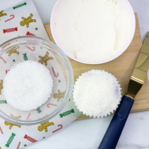Cupcake topped with a thin layer of white buttercream being dipped into white sanding sugar to create a snowy surface.