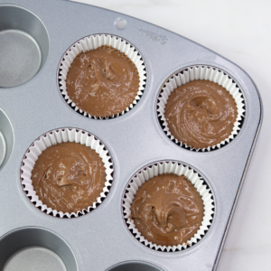 Unbaked chocolate cupcake batter in white paper liners inside a metal muffin tray.