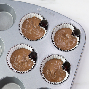 Muffin tray with chocolate batter and small metal foil balls placed at the edge of each cupcake liner to create a shaped dip.