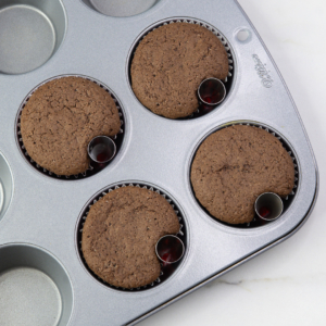 Freshly baked chocolate cupcakes in a muffin tray, each with a small round indentation where the metal foil balls were placed.