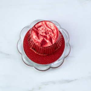 Cupcake dipped upside down into a dish of red sanding sugar to coat the buttercream evenly.