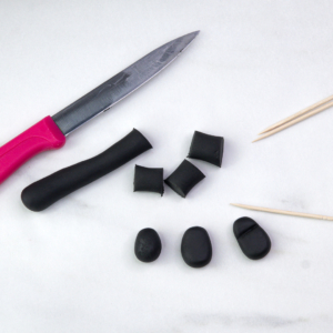 Black fondant rolled and cut into boot shapes, with a small knife and toothpicks beside the pieces.