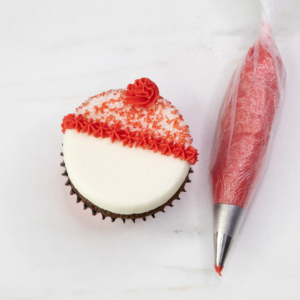 Piped red buttercream hat topped with sanding sugar on a snowman cupcake ready for details
