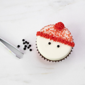 Using tweezers to place black sprinkle eyes onto the smooth buttercream snowman face