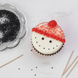 Using a cocktail stick to add the snowman’s smile by placing black pearl sprinkles evenly.