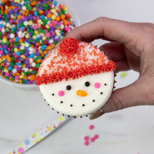 Finished snowman cupcake with red hat, pink cheeks, carrot nose, and textured trim.