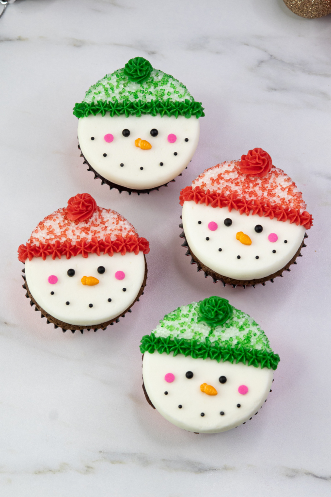 Four decorated snowman cupcakes arranged neatly with colourful hats and cheerful faces