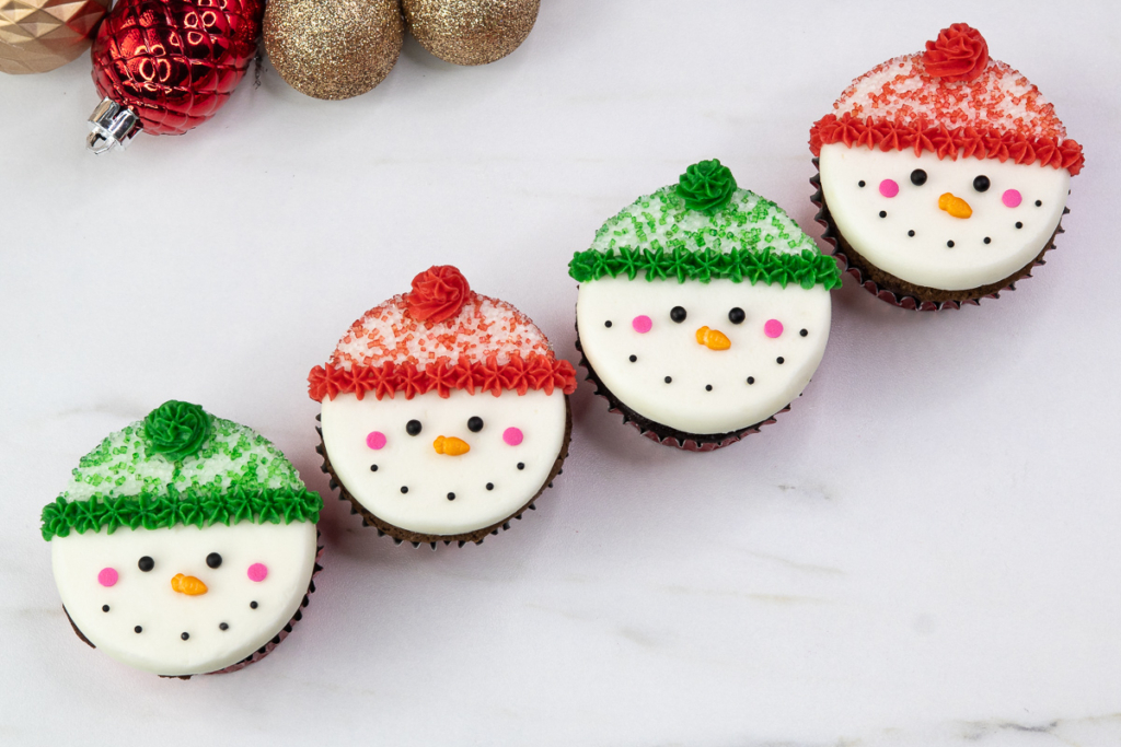 Snowman cupcakes arranged on a white background showcasing their smooth faces and colourful hats.