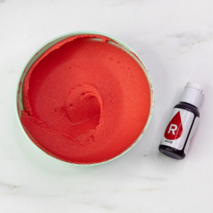 A bowl of bright red buttercream and a bottle of gel colour.