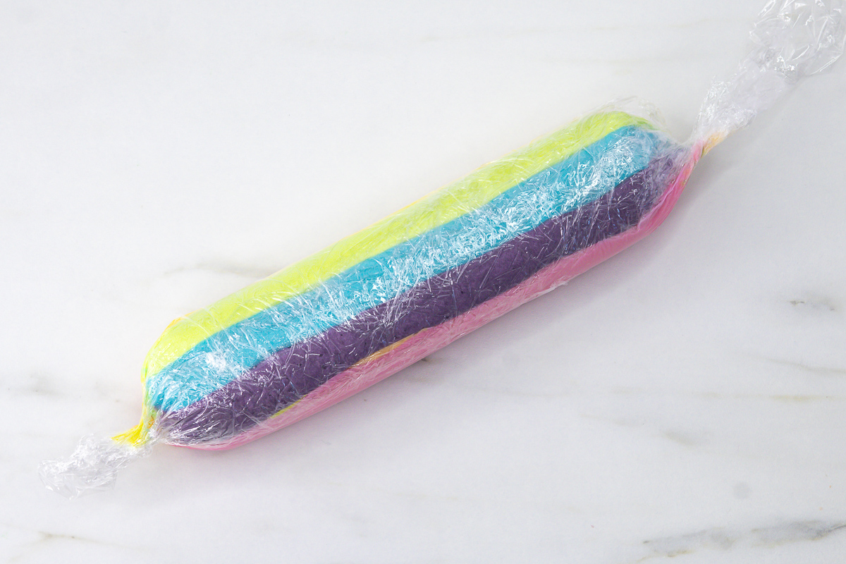 Trimmed multicoloured buttercream sausage beside a piping bag fitted with a Wilton 8B piping tip.