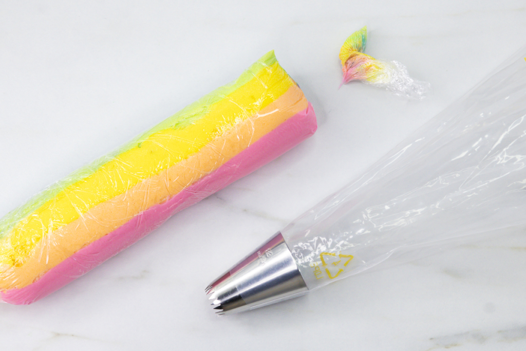 Trimmed multicoloured buttercream sausage beside a piping bag fitted with a Wilton 8B piping tip.