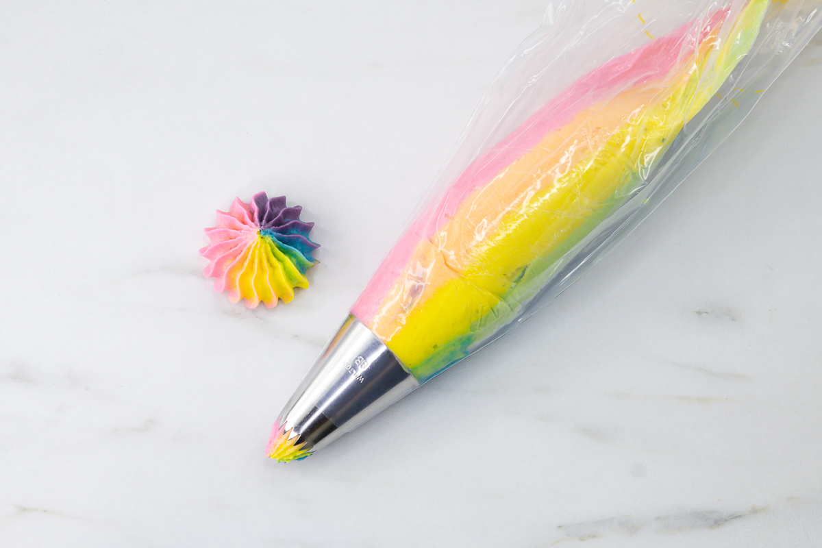 Multicoloured buttercream loaded into a piping bag fitted with a Wilton 8B tip with a test swirl piped beside it.